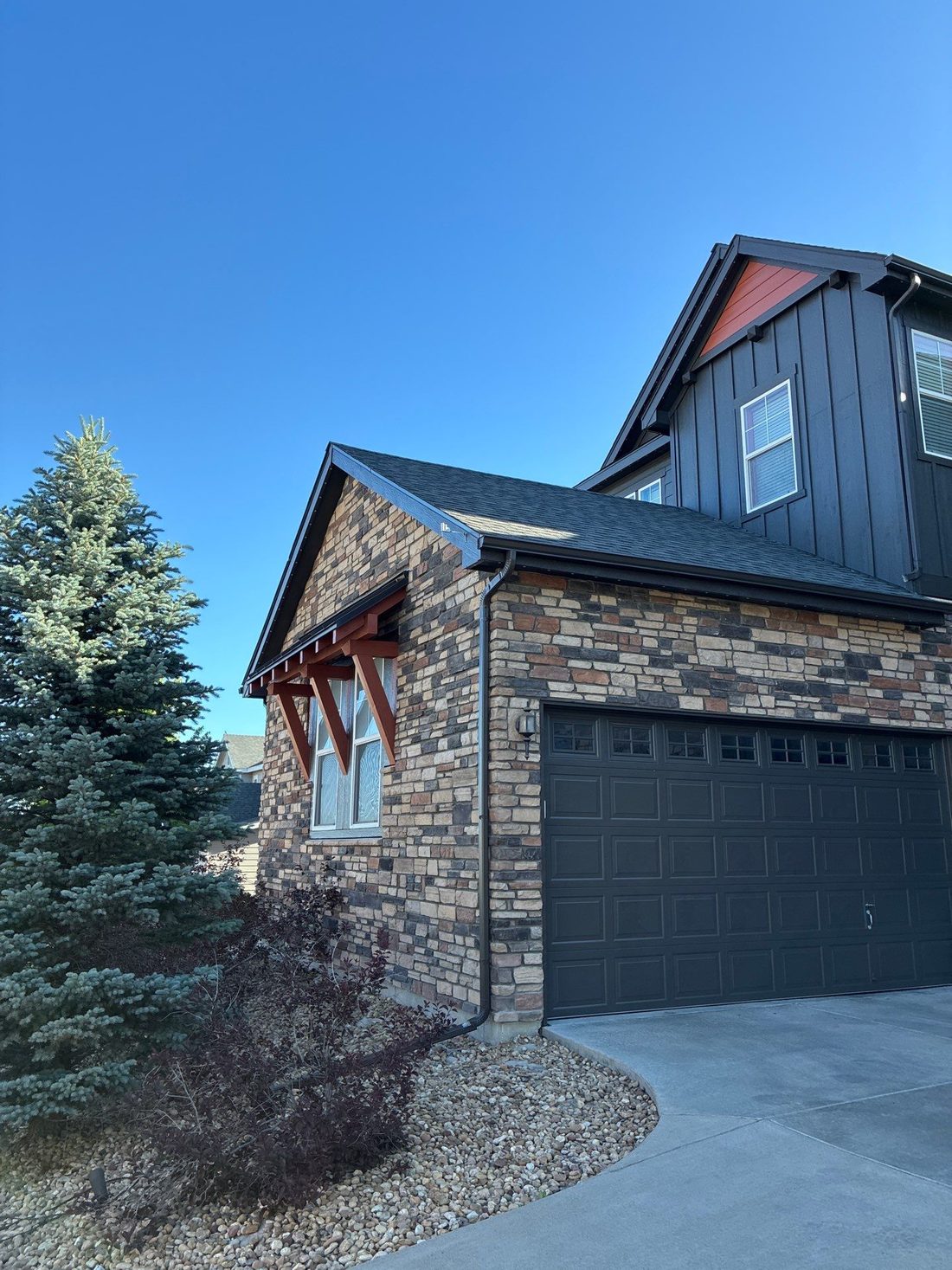 Charcoal board-and-batten siding and burnt-orange corbels paired with a multi-tone stone base on a Castle Rock home