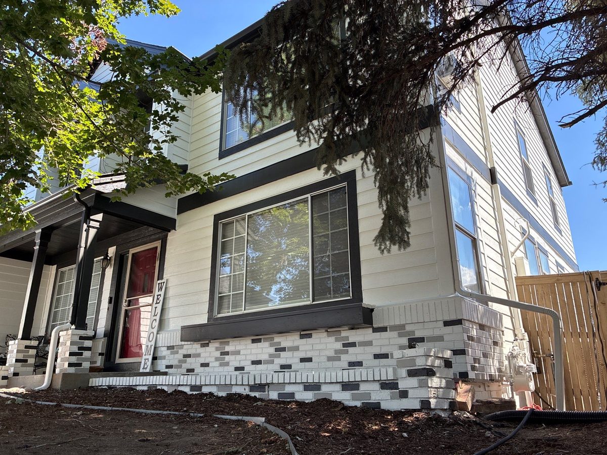 Castle Rock home with a warm white body, black trim, bold red front door, and whitewashed brick base
